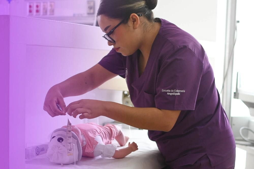 Healthcare worker in purple scrubs examining or treating a newborn baby under a pink heat lamp in a medical incubator