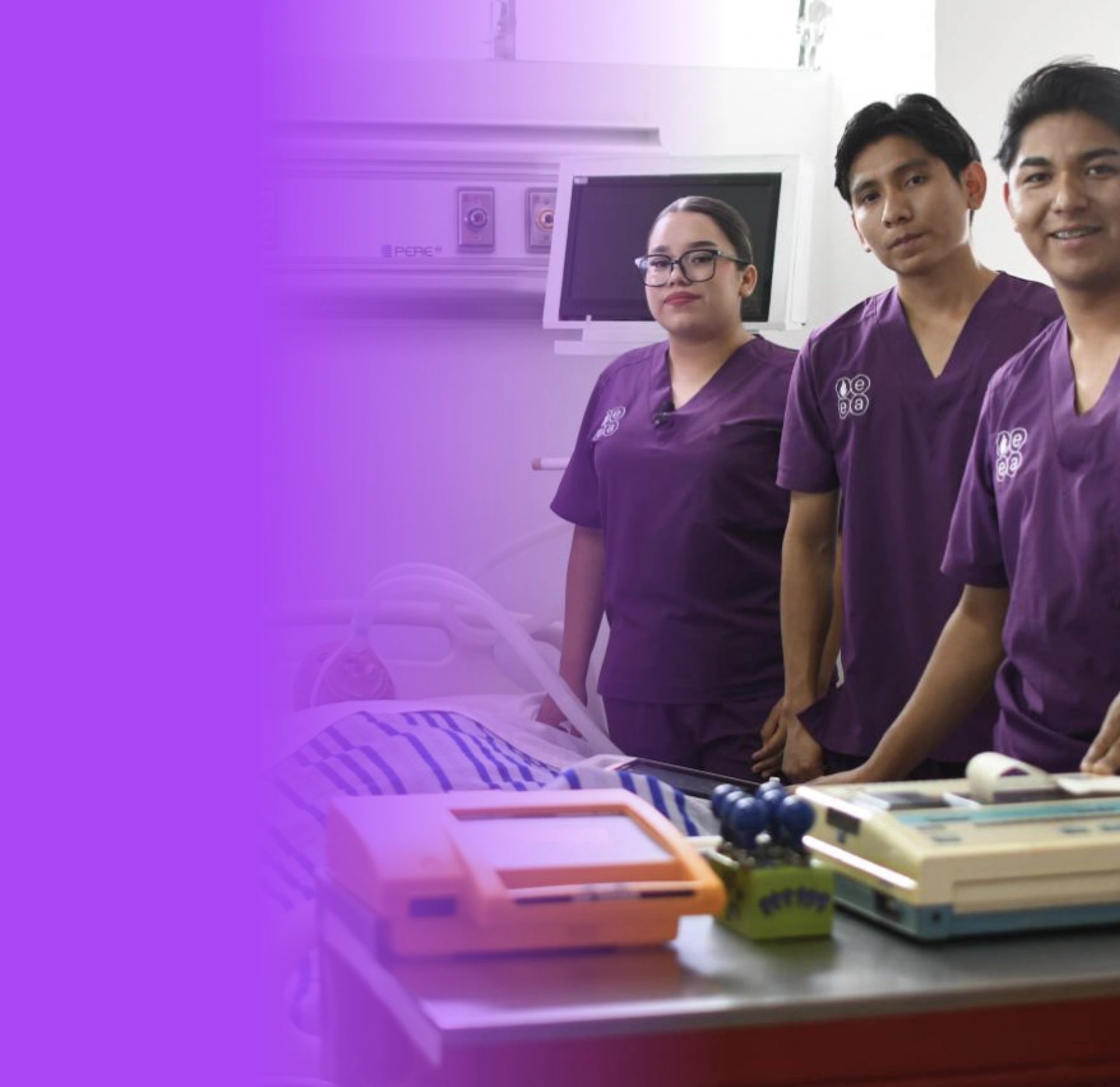 Three medical professionals in purple scrubs standing at a desk with equipment and documents in a clinical setting