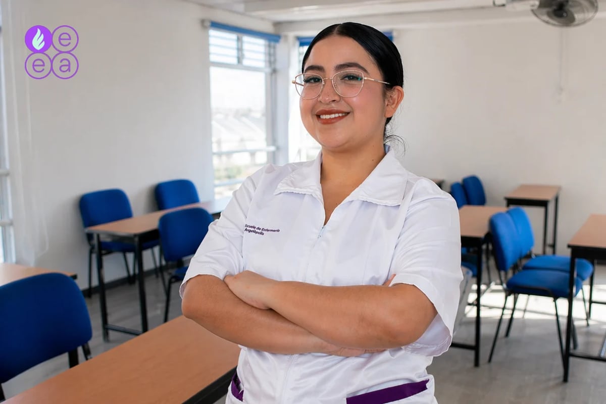 Professional woman wearing glasses and white shirt standing in a classroom with blue chairs and wooden tables in the background
