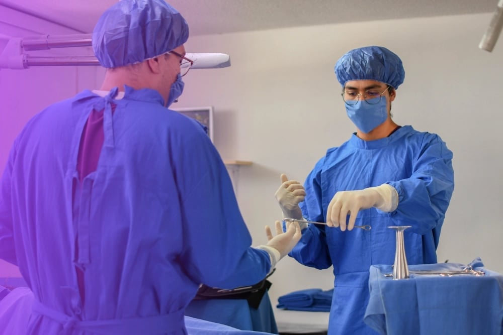 Two medical professionals in blue surgical attire and caps prepare sterile instruments for an operating room procedure