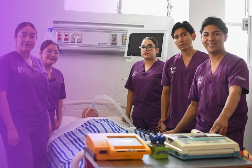 Five healthcare workers in purple scrubs standing together in a medical facility with medical equipment and supplies on a table