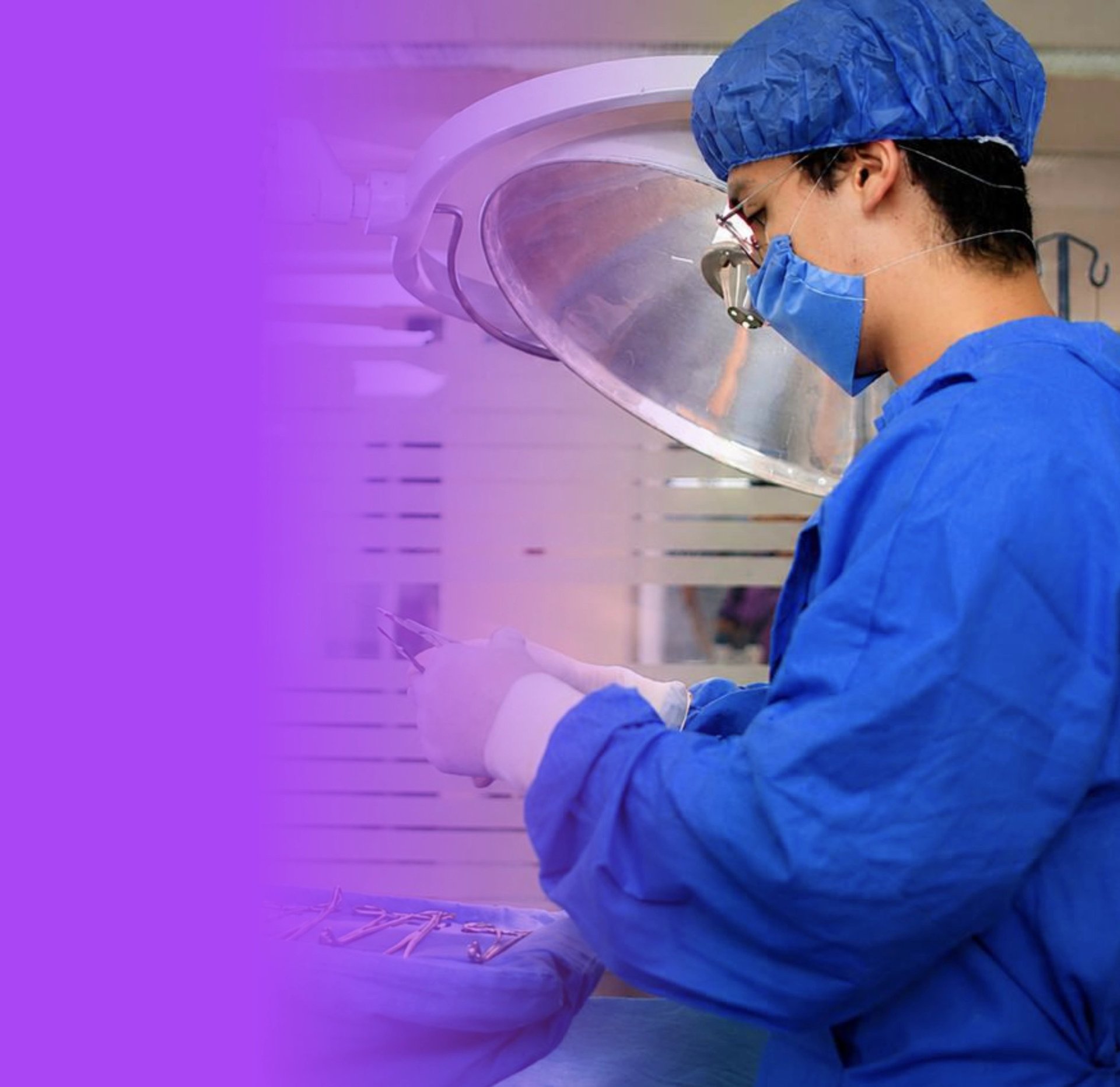Surgeon in blue scrubs and surgical mask working under an overhead operating light in a medical facility