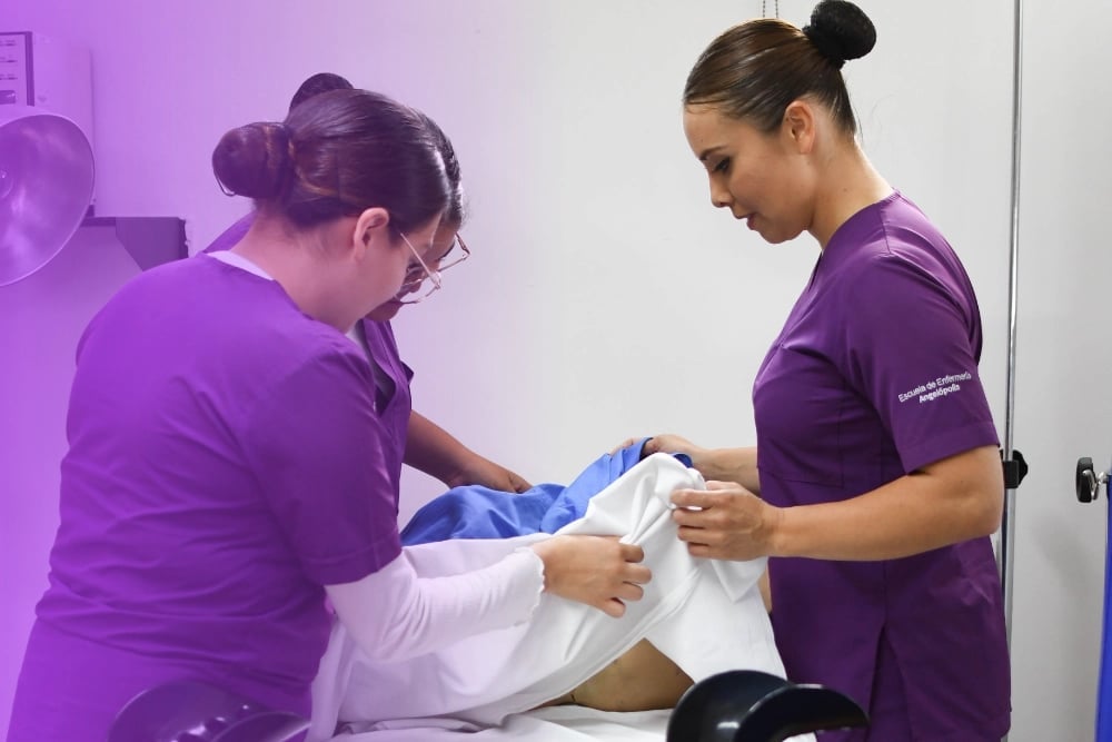 Two healthcare professionals in purple scrubs examining a patients leg with blue medical wrap in a clinical setting