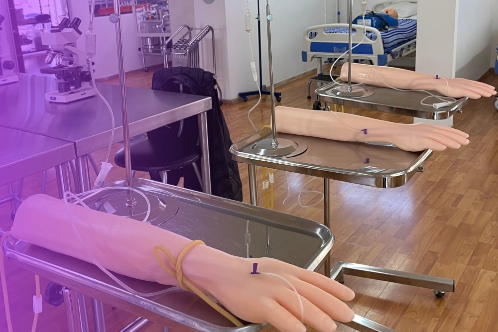 Training room with mannequin hands and arms displayed on tables under purple lighting for medical or phlebotomy practice