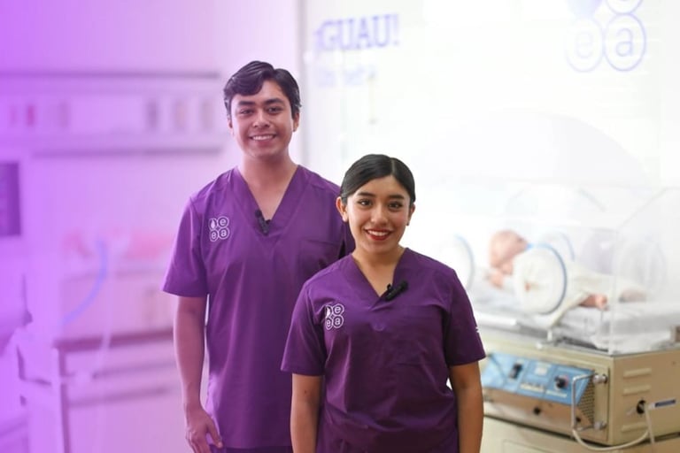Two healthcare workers in purple scrubs smiling in a modern medical facility with equipment visible in the background
