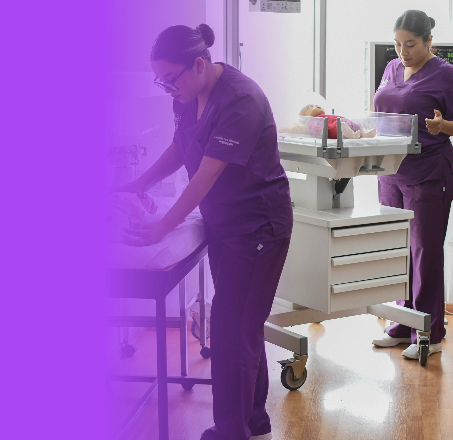 Healthcare worker in purple scrubs attending to a patient in a medical examination room with equipment and supplies visible