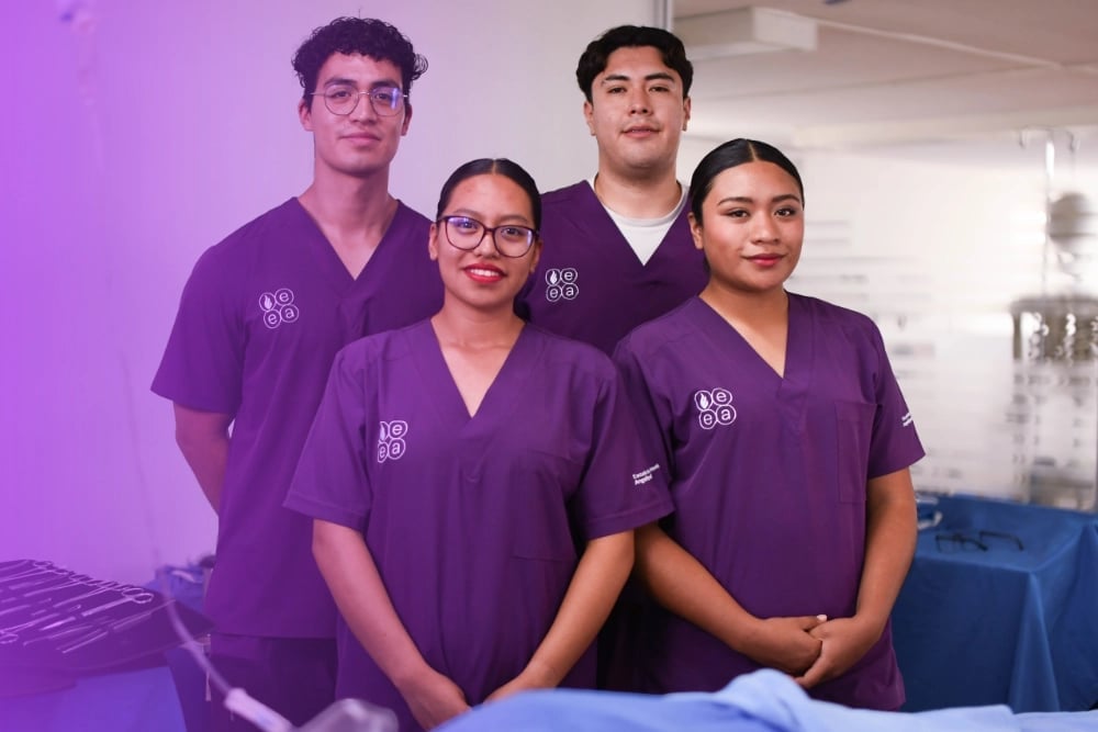 Four healthcare workers in purple scrubs smiling at camera in a medical facility