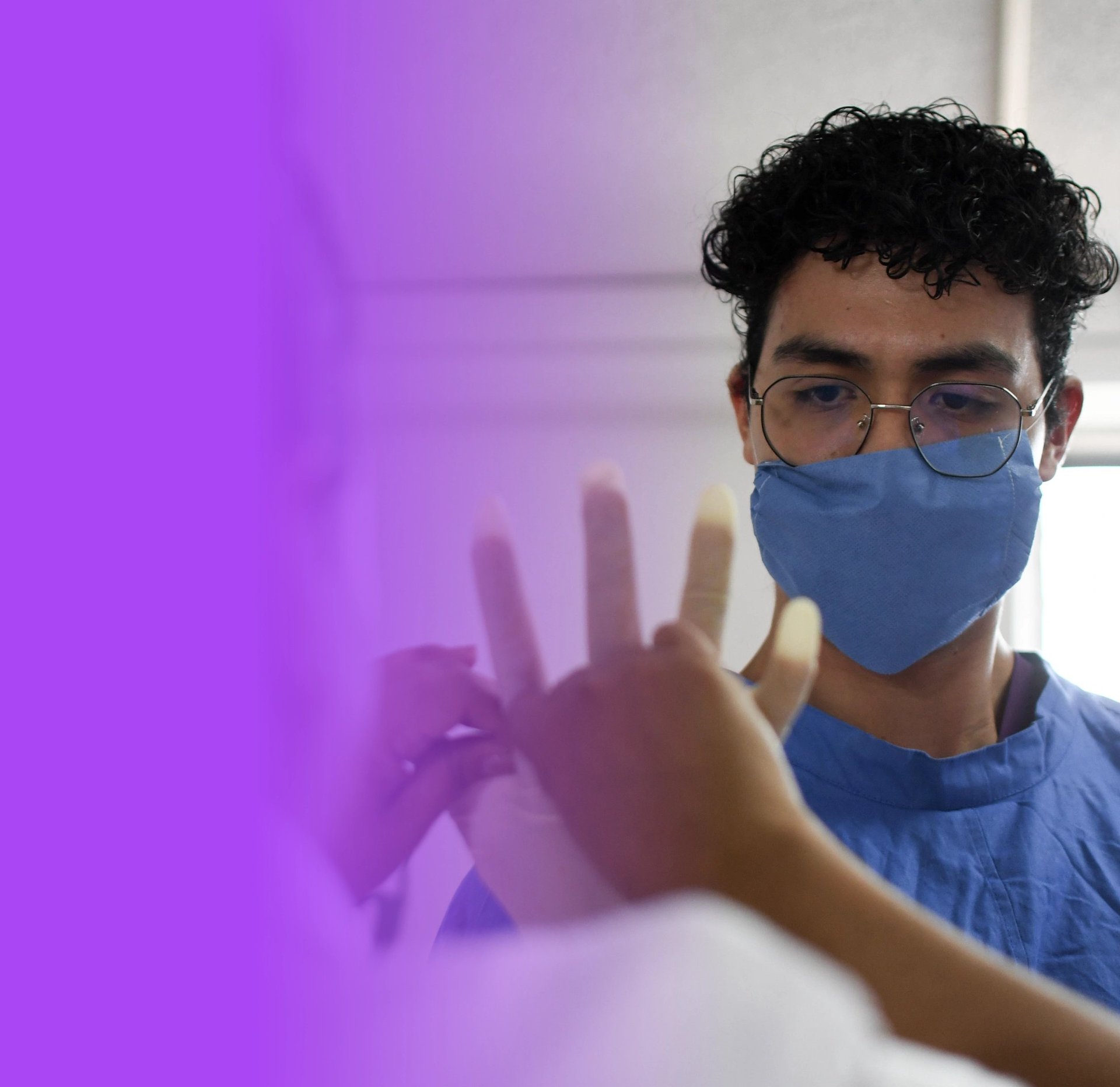 Person wearing blue face mask and glasses touching a purple frosted glass panel with hand visible through translucent material