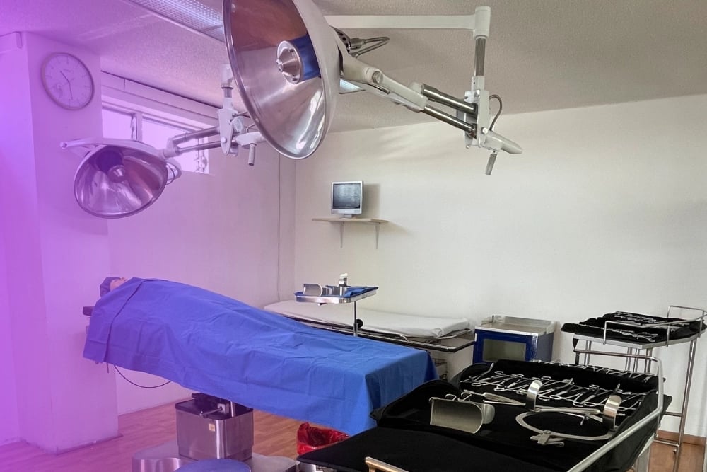 Medical or surgical operating room with overhead lights, surgical bed covered in blue drape, and equipment on right side under purple and white lighting