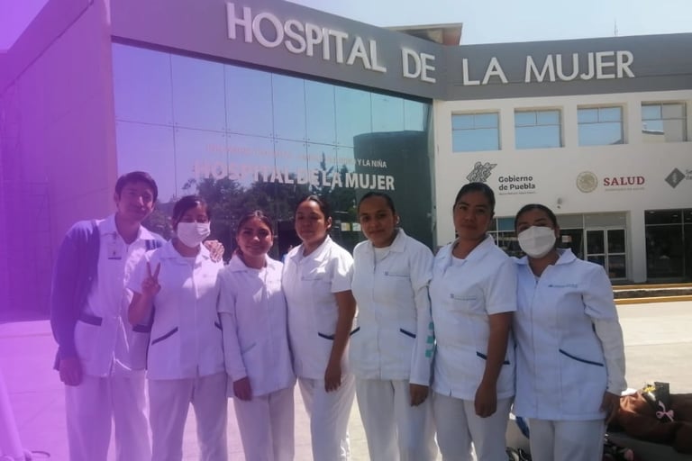 Group of healthcare workers in white uniforms standing in front of Hospital de la Mujer building entrance