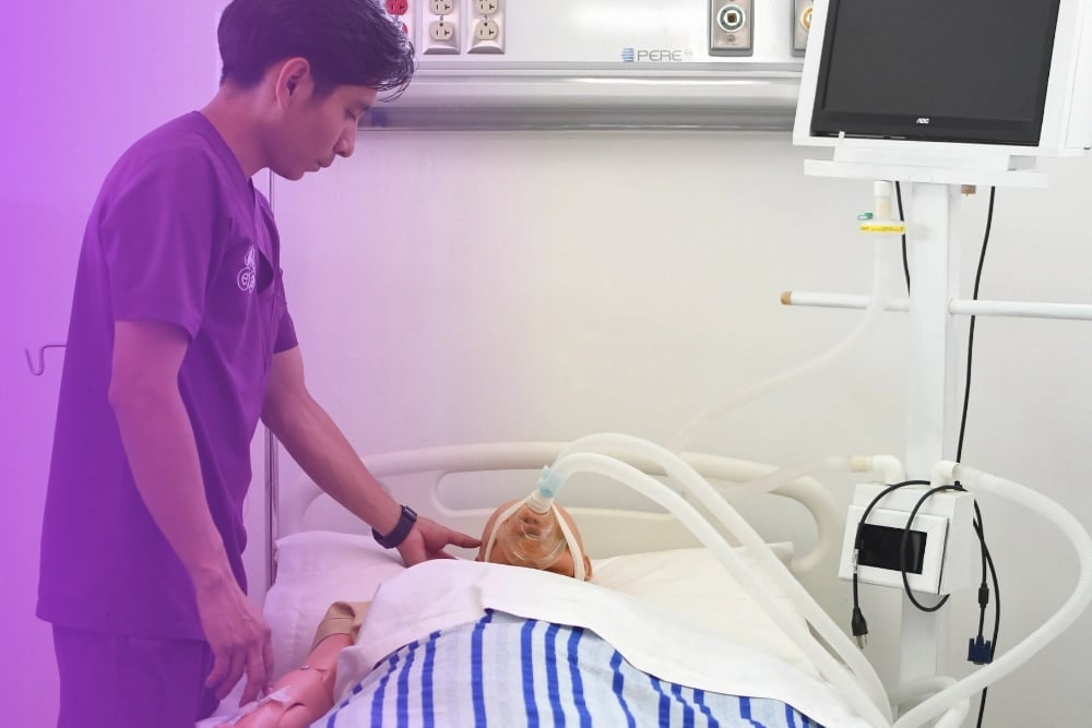 Healthcare worker in purple scrubs examining a newborn baby in hospital bassinet with medical equipment visible